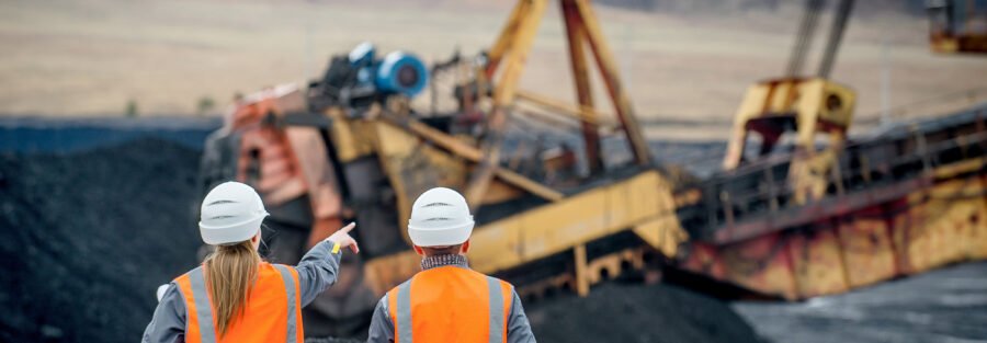 Monitoring to Prevent Patterns of Violations: two mine workers in orange safety vest overlooking a coal operation.