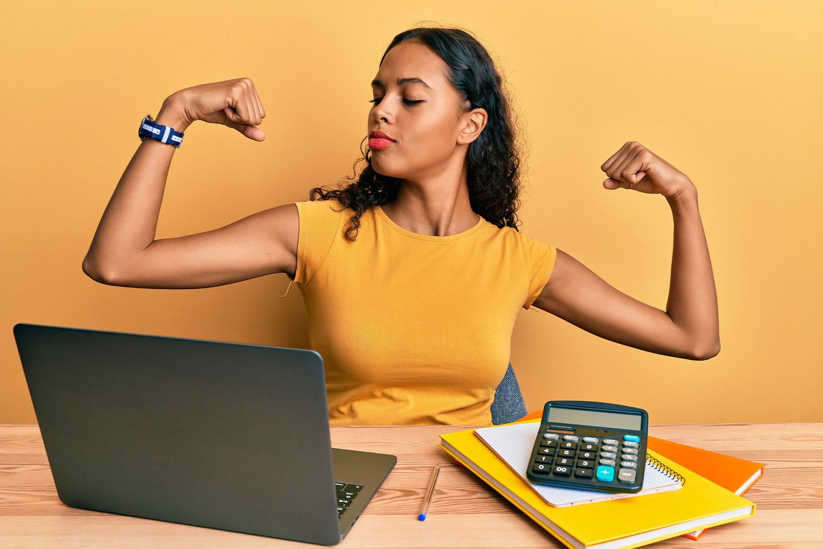 rethinking employee benefits: a professionally-dressed business woman flexing her biceps while sitting at her laptop.