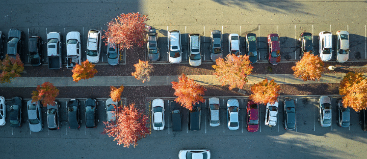 Cars parked in an outdoor lot surrounded by fall foliage.