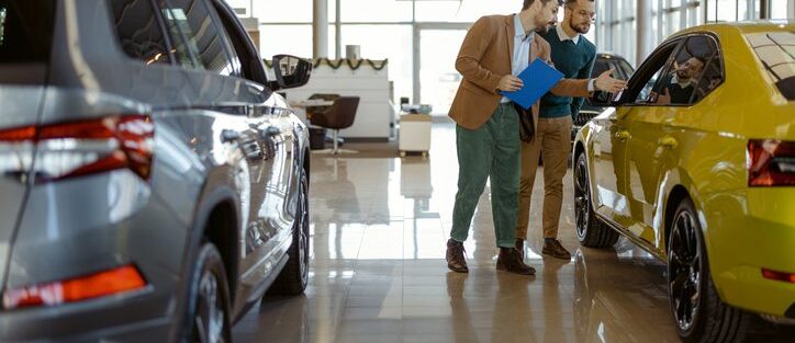 A car insurance agent showing a yellow car to a customer inside a dealership.