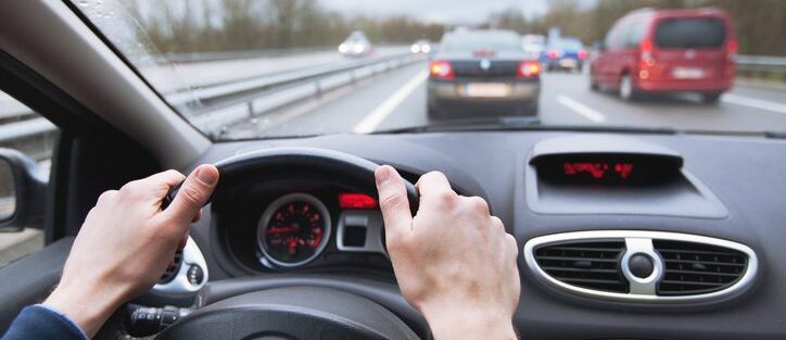 Driver holding a steering wheel on a busy highway in traffic, illustrating driving with g2 license restrictions.