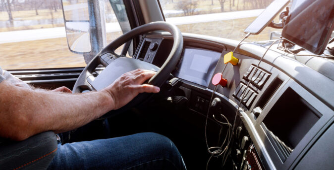 Driver in cabin of big modern truck vehicle on highway